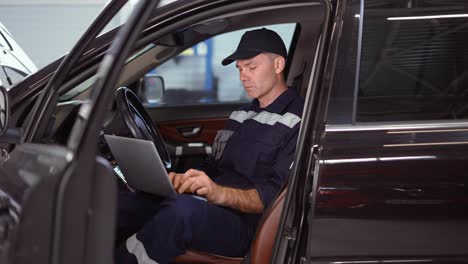 mechanic working on laptop in auto repair service inside the car