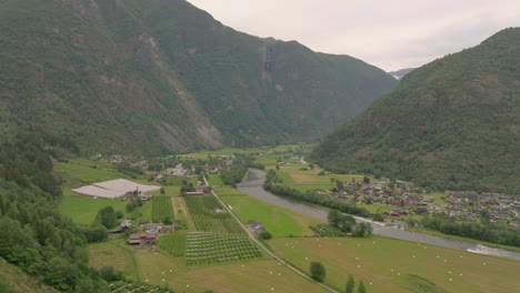 Pintoresco-Pueblo-Pintoresco-Del-Valle-De-Laerdal-Junto-Al-Río-Laerdalselvi-Y-La-Plantación-De-Huertos-De-Manzanas,-Toma-Aérea-Descendente