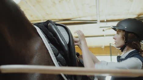 woman saddling a horse in a stable