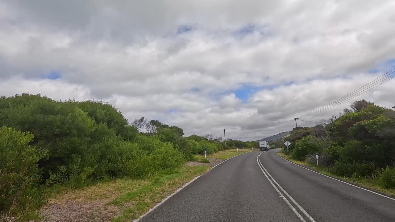 A 15-second drive along the Great Ocean Road, showcasing lush greenery, coastal views, and a winding road under a cloudy sky