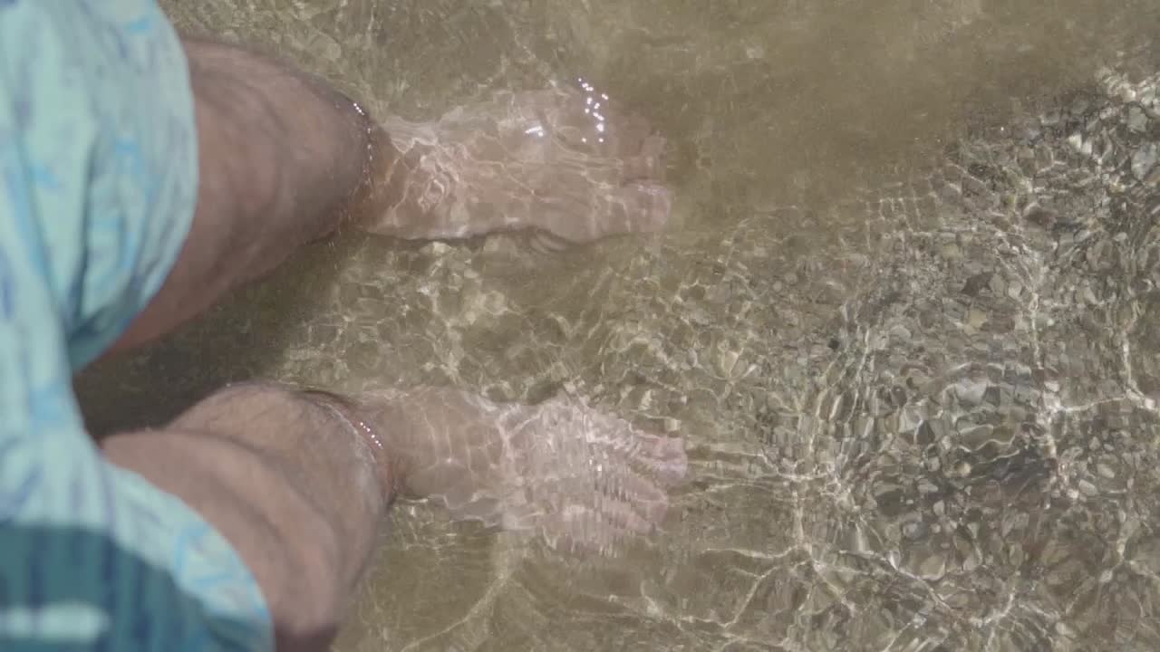 Vista a volo d'uccello dei piedi di un uomo in acqua limpida in spiaggia.