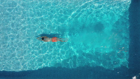 overhead drone shot of man diving into outdoor pool and swimming underwater