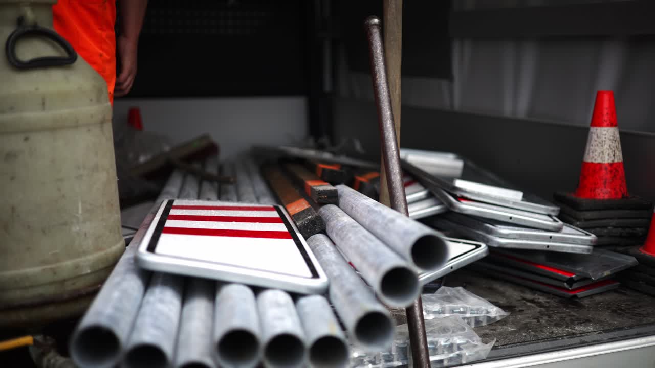 Safety worker in orange coverall pants reaches intotruck full with roadwork safety signs