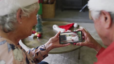 pareja caucásica mayor sonriente usando un teléfono inteligente para una videollamada de navidad con un niño en la pantalla