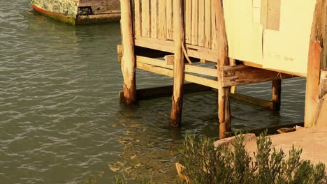 Fesselnde-Standbilder-Einer-Szene-Am-Wasser,-Während-Die-Kamera-Das-Allmähliche-Eintauchen-Eines-Holzhausfundaments-In-Das-Ruhige-Wasser-Darunter-Einfängt