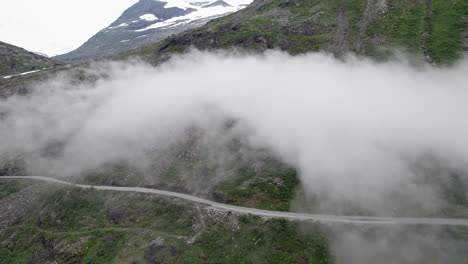 Toma-Aérea-De-Los-Trollstigen,-Noruega-Mientras-La-Carretera-Pasa-Bajo-Una-Nube.