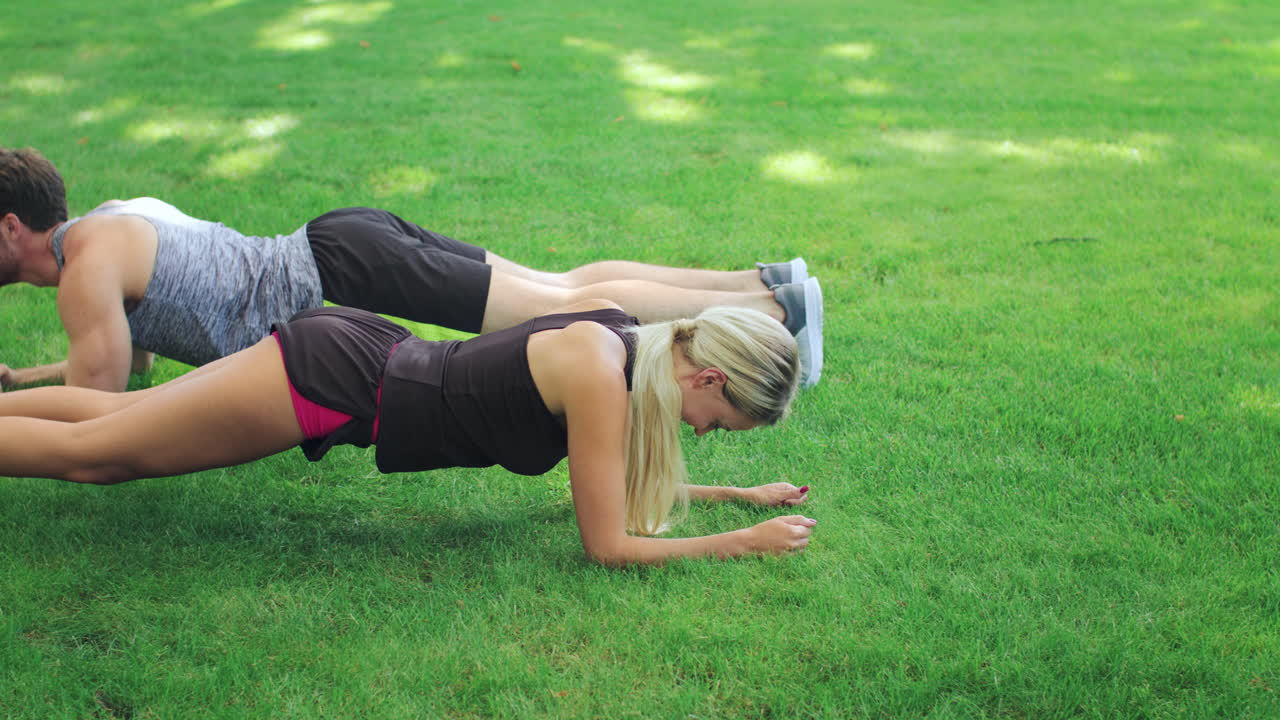pareja de fitness hombre y mujer entrenando ejercicio de tabla en el césped en el parque de verano