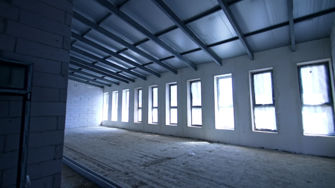 Entering the spacious attic room with multiple narrow windows and brick walls. Interior of the new building.