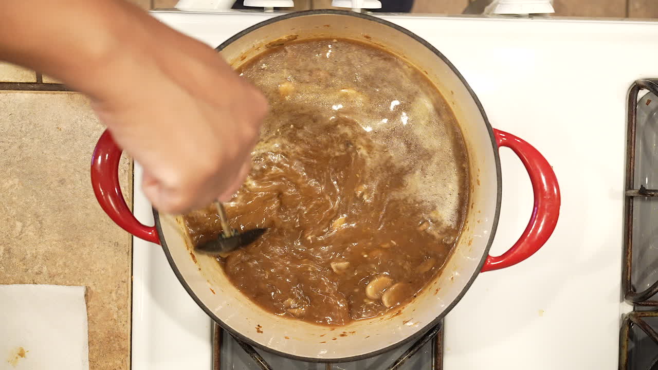 Stirring wild rice mushroom soup as it boils in a pot on the stove in slow motion - overhead view WILD RICE SERIES