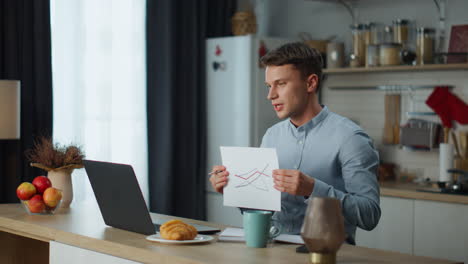 Teacher-conducting-online-training-at-kitchen.-Man-showing-economic-graphs.