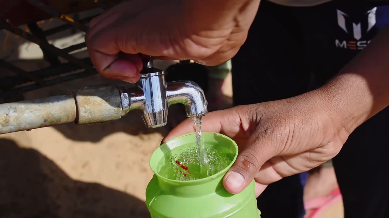 una persona llena una jarra de plástico para beber agua del grifo del camión cisterna en el lugar del festival del desierto