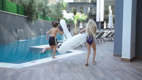 Niña-Y-Niño-Corren-Junto-A-La-Piscina-Con-Juguetes-De-Piscina-En-Sus-Manos