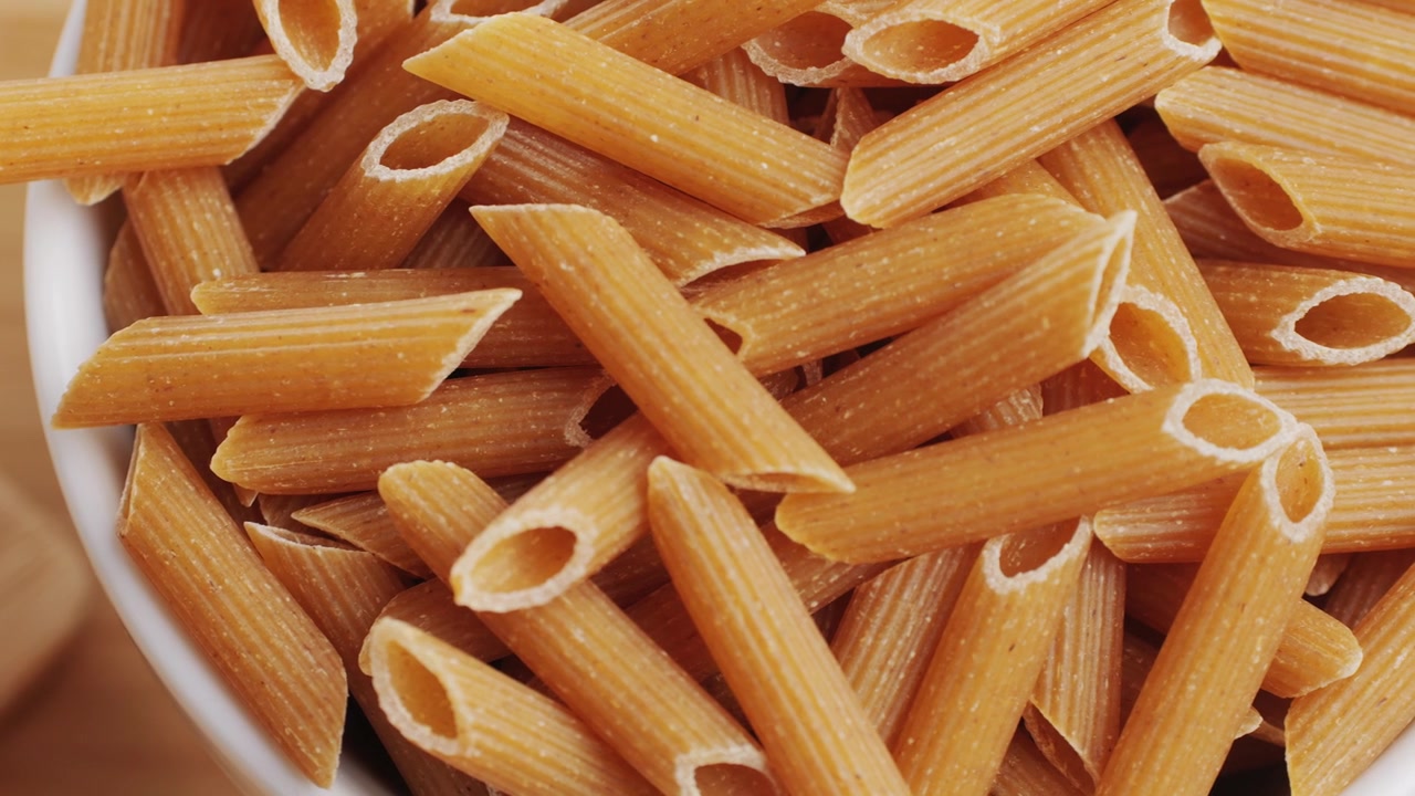 Pasta integrale biologica, maccheroni di semola di grano duro, penne rigate crude in una ciotola di legno. Filmato 4k di alta qualità