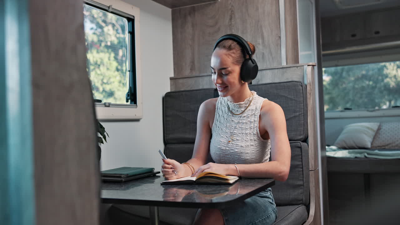 Young Woman with Headphones Writing in Notebook Inside Camper Van