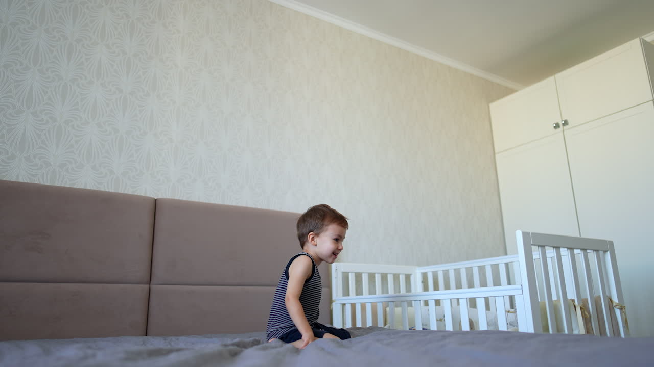 Caucasian toddler boy jumps on the large parents' bed. Energetic kid having fun at home.