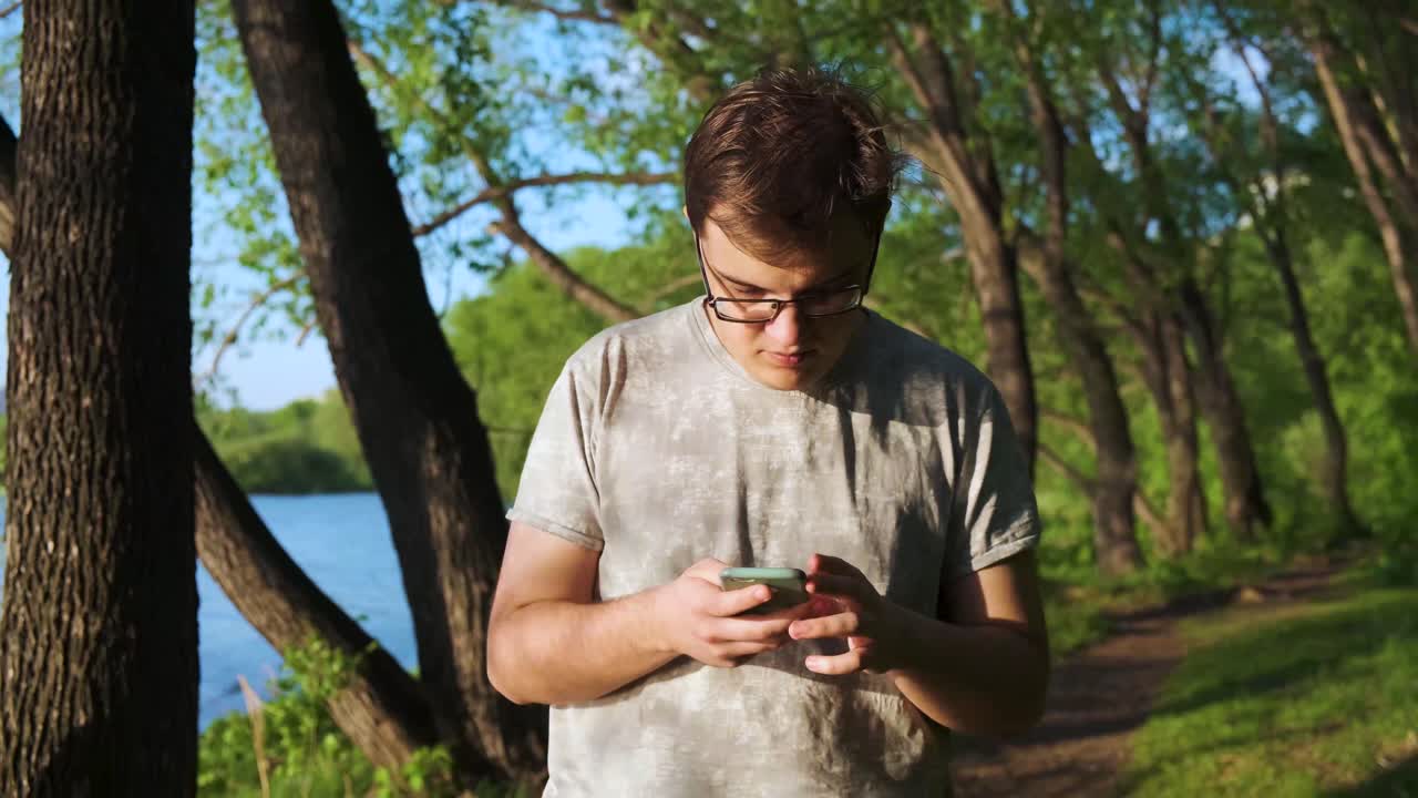 Young man using smartphone in a park by the river