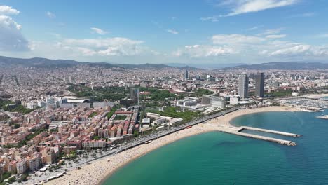an expansive aerial panorama showcases barceloneta beach in barcelona, spain, stretching along the vibrant city skyline with mountains in the distant backdrop.