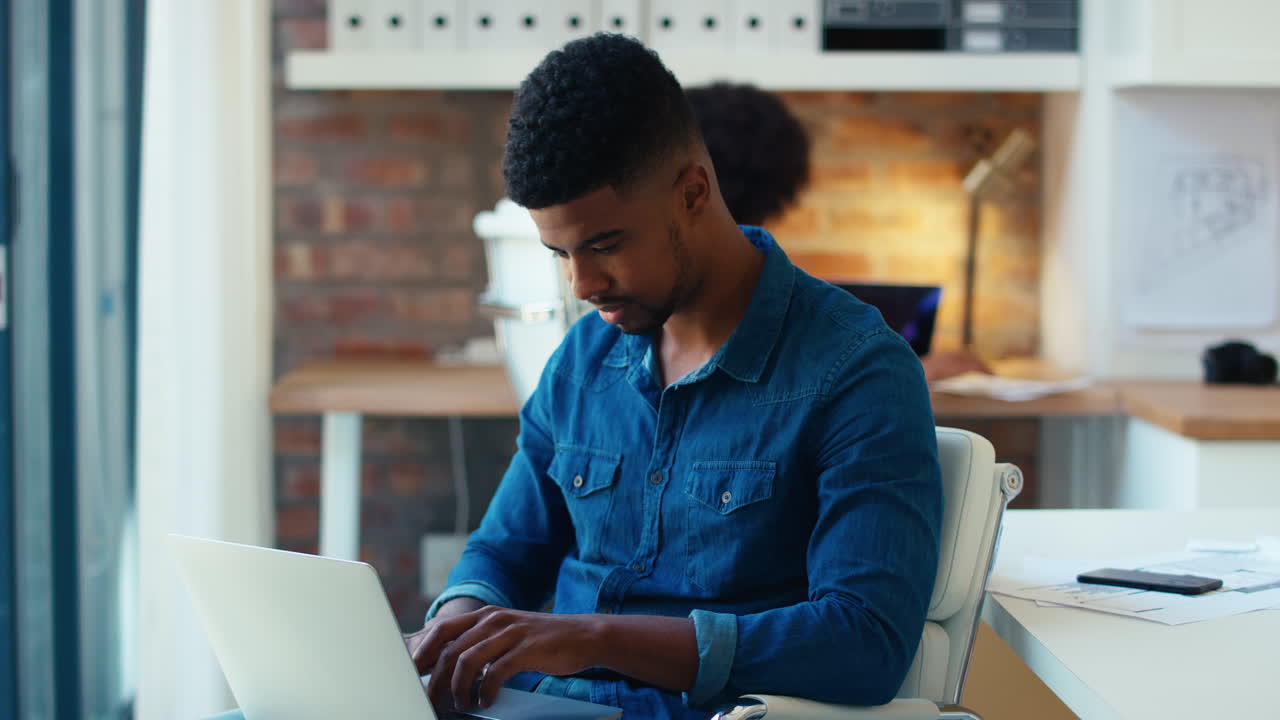 Young Businessman Working On Laptop At Desk In Modern Office