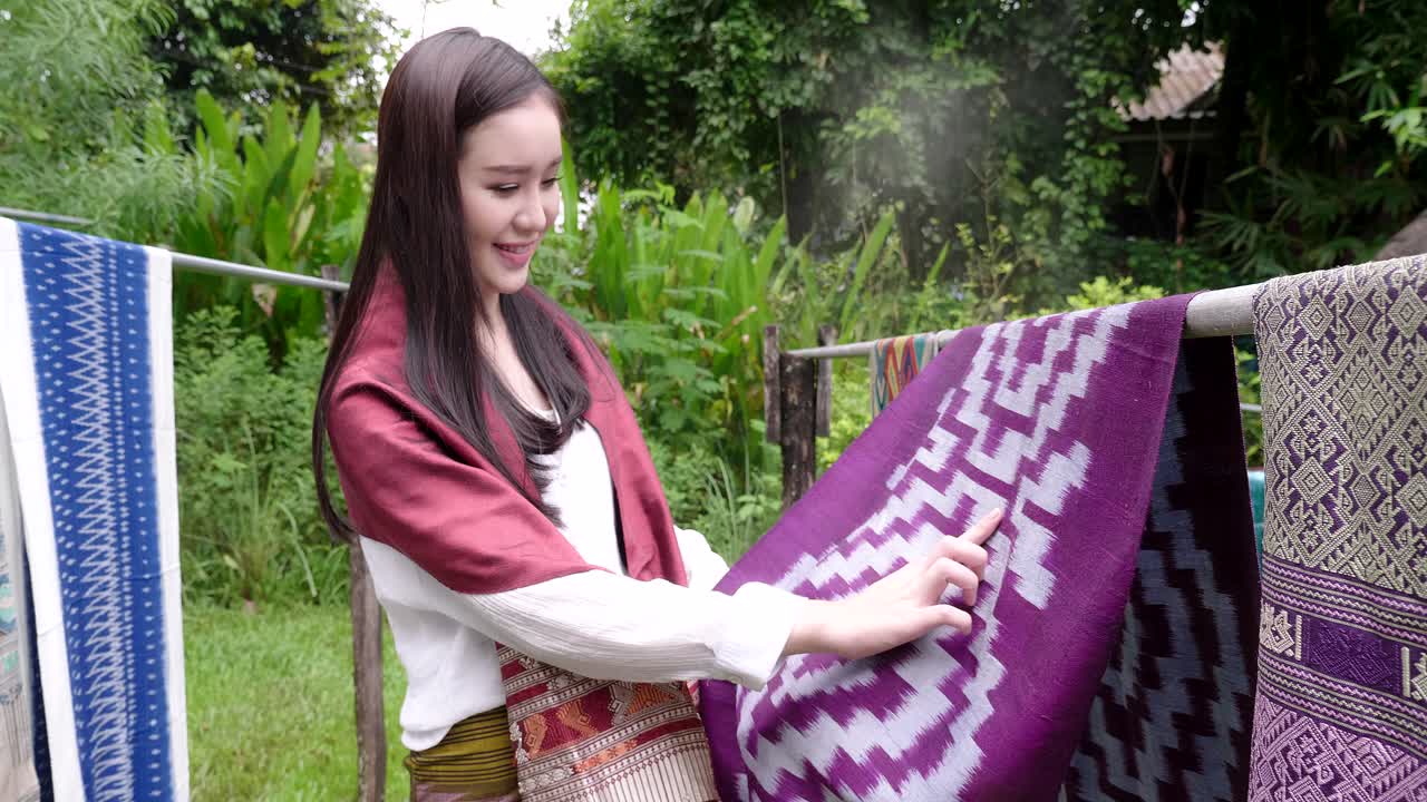 Thai Woman in Traditional Garments Viewing Handwoven Textiles