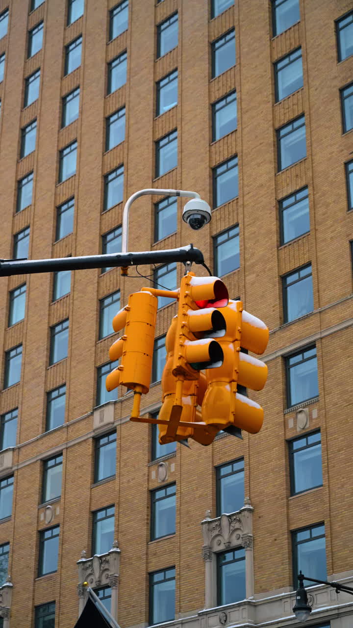 Semaforo e telecamera innevati a Manhattan. Semaforo giallo e telecamera di sorveglianza ricoperti di neve con la classica facciata di un edificio di Manhattan sullo sfondo