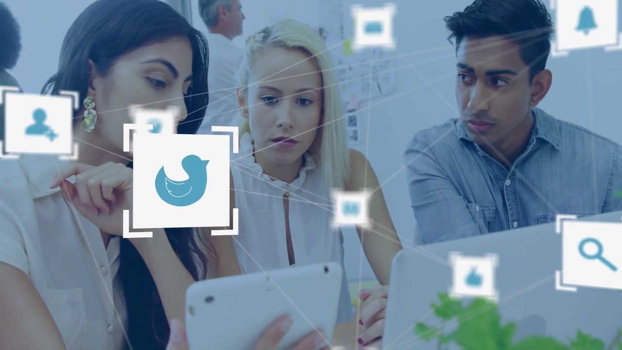 Team leaning over tablet and laptop, woman pointing causing moving social icons guiding marketing