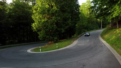 Drone-shot-of-a-moving-sports-car-taking-a-sharp-turn-in-a-green-forest-in-summer