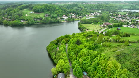 a broad aerial view of a lakeside town surrounded by green hills, showing houses, roads, and a tranquil lake