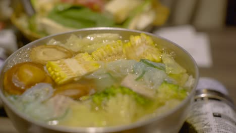 various vegetables bubbling in boiling hot asian hotpot soup, filmed as slow motion close up shot