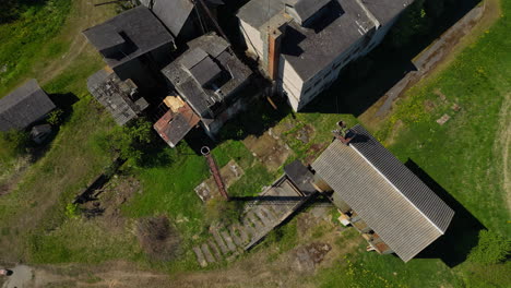 aerial drone top down shot over an old village building with black roof surrounded by green grass on a sunny day