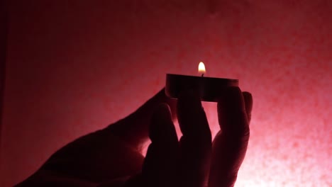 Hand-holding-single-tea-light-in-red-lighting