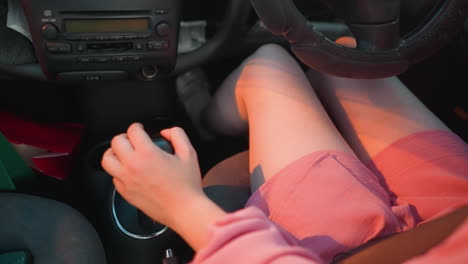 leg view of woman shifting gear in her car, moving it forward and backward with visible shopping bag and coffee cup near the gear shift, shadows of passing cars reflect on her while driving