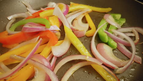 salteando cebollas en rodajas con pimientos rojos, verdes y amarillos en una sartén antiadherente