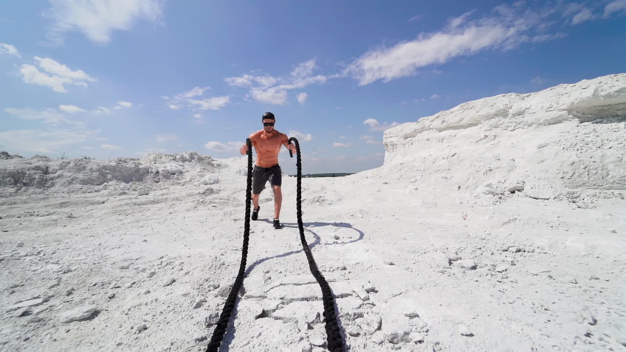 Man working out with fitness rope. Athletic muscular man doing workout with battle ropes