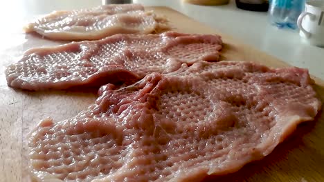 seasoning sliced and tenderized pork loins on a chopping board with coarse sea salt