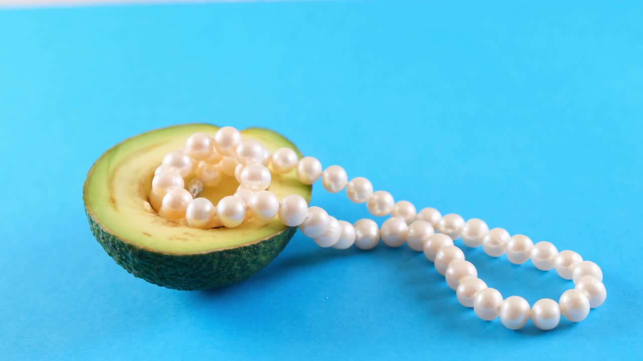 Mezzo avocado fresco con perle su sfondo blu. Design alimentare alla moda