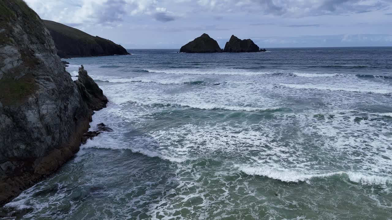 Video aereo con drone che mostra le onde infrangersi lungo la costa rocciosa a Bedruthan Steps in Cornovaglia, Inghilterra, con faraglioni, scogliere, il movimento dell'oceano e uno spettacolare paesaggio costiero