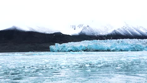 Glacier-surrounded-by-snow-capped-mountains-and-ice-blocks-in-the-Arctic-Sea