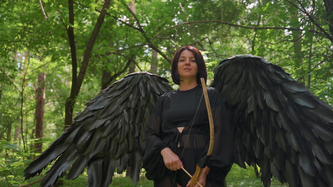 Forest warrior with large black wings stands confidently holding bow in sunlit woods, calm expression glowing in green light, powerful fantasy presence radiating courage