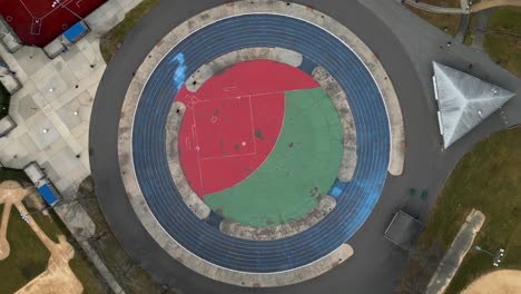 a top down view directly above a circular track and sports field in an empty park on a cloudy day