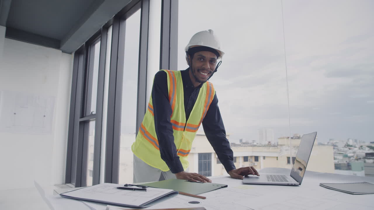 Foreman Turning to Camera while Working on Laptop on Site