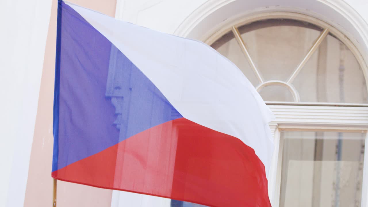 Czech flag waves in daylight breeze before arched window, soft natural lighting, steady camera