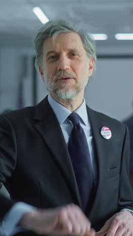 businessman with badge speaks on camera and calls for voting in modern polling station. portrait of man, united states of america elections voter. background with voting booths. concept of civic duty.