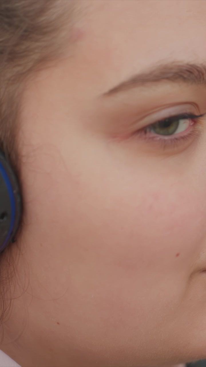 Dita afferrano un oggetto accanto a vestiti scuri e capelli castani. Smalto rosa chiaro visibile su pollice e indice. Lo sfondo mostra forme indistinte senza dettagli chiari.