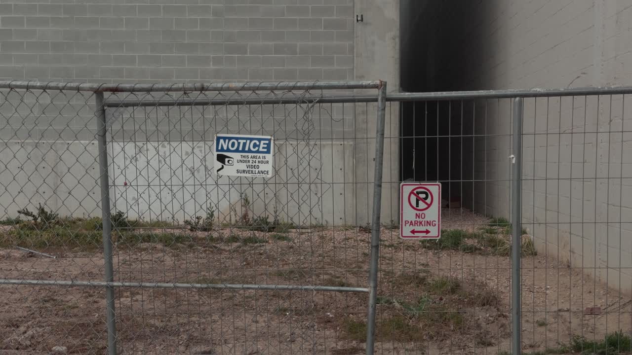 Handheld shot of fenced industrial entrance with warning signs and restricted access area