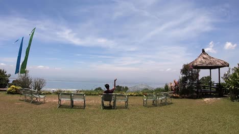 guy sitting on a bench looking out in the vast expanse atop penang hill waving