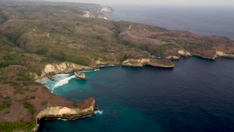 Toma-Aérea-De-Las-Olas-Del-Océano-Turquesa-Rompiendo-La-Costa-De-La-Playa-Rota-Famoso-Lugar-Turístico-En-La-Isla-De-Nusa-Penida,-Indonesia