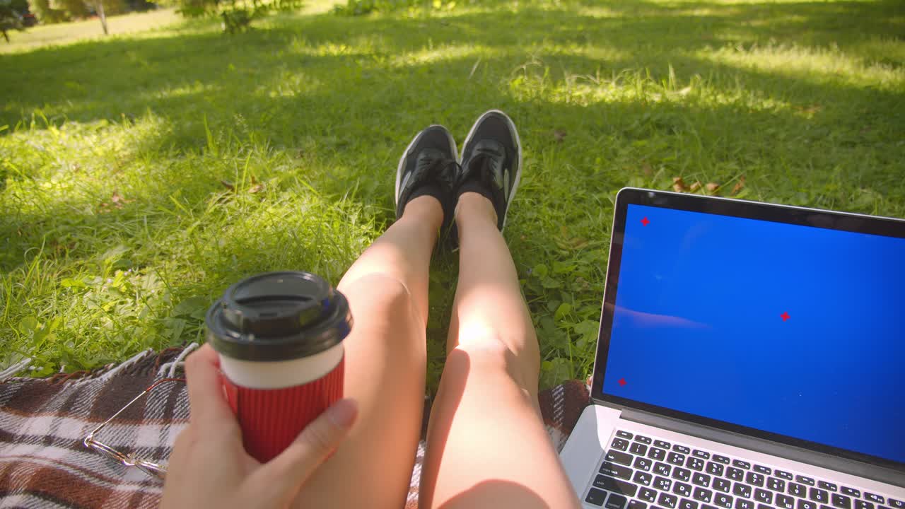 야외 공원에서 파란 화면의 노트북을 사용하여 커피를 들고 카에 앉아있는 젊은 예쁜 백인 여성 다리의 소녀의 클로즈업 초상화