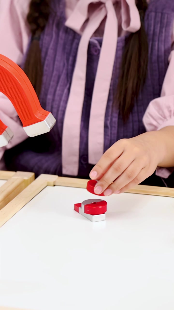 Primo piano delle mani degli studenti che manipolano magneti su un tavolo bianco durante una lezione di fisica
