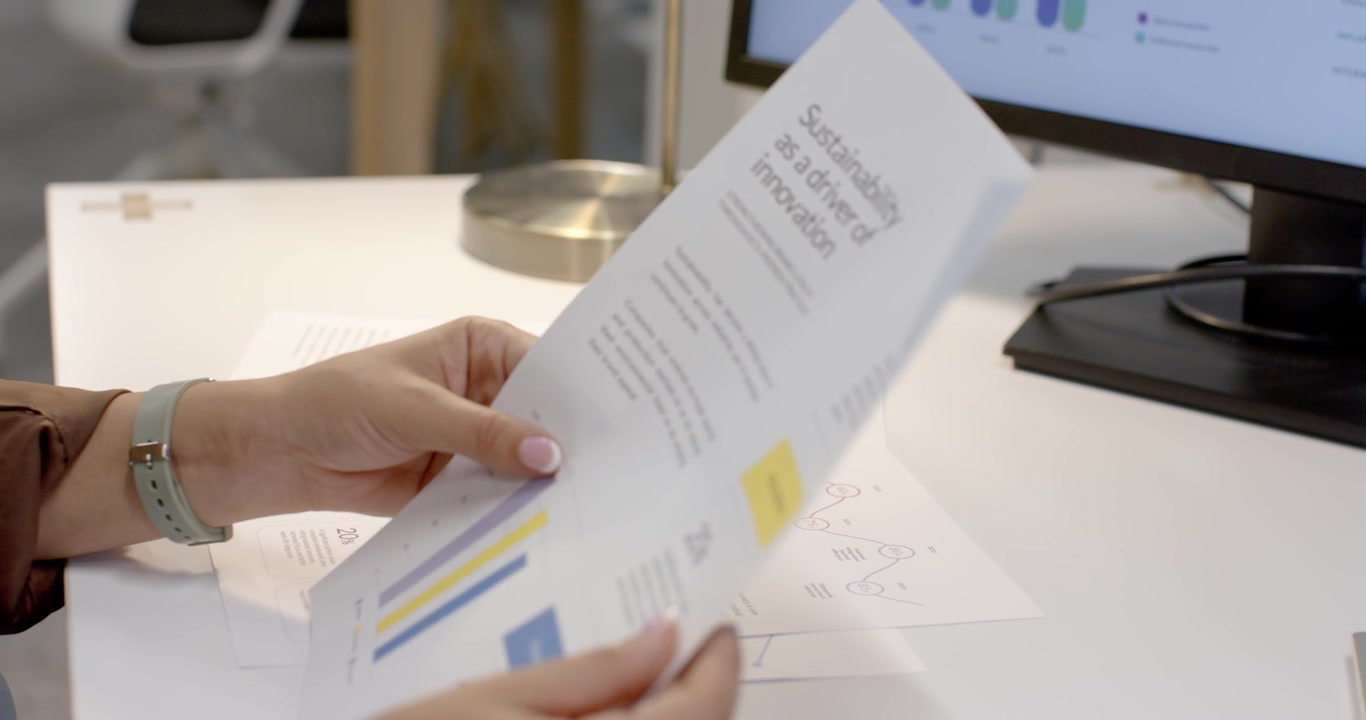 Left hand reaching, Asian woman flipping colorful report sheets at white desk, preparing report