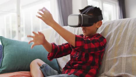 Happy-asian-boy-at-home,-sitting-on-couch-in-living-room-wearing-vr-headset